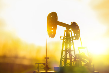 silhouette of an oil drilling pump against a background of sun rays in the sunset