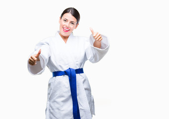 Young beautiful woman wearing karate kimono uniform over isolated background approving doing positive gesture with hand, thumbs up smiling and happy for success. Looking at the camera, winner gesture.