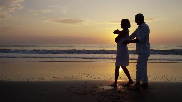 Silhouette of retired Caucasian couple dancing on the ocean beach at sunset