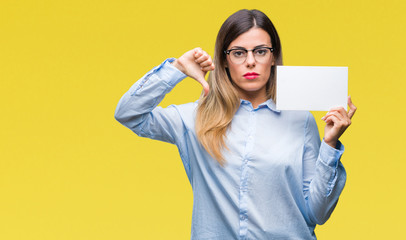 Young beautiful business woman holding blank card over isolated background with angry face,...