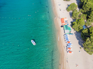 Fototapeta premium Drone aerial view of sea shore, sandy beach and blue water. Boat near beach with lot of sunshades