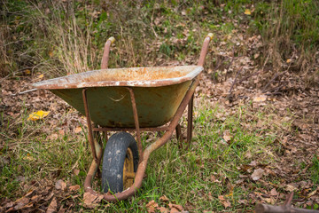 Rusty and abandoned wheelbarrow in a garden, with the wheel still in place.