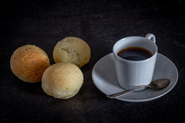 Brazilian homemade cheese bread, AKA 'pao de queijo' in a rustic background and a cup od coffee