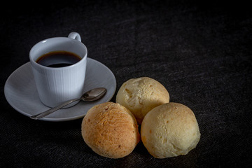 Brazilian homemade cheese bread, AKA 'pao de queijo' in a rustic background and a cup od coffee