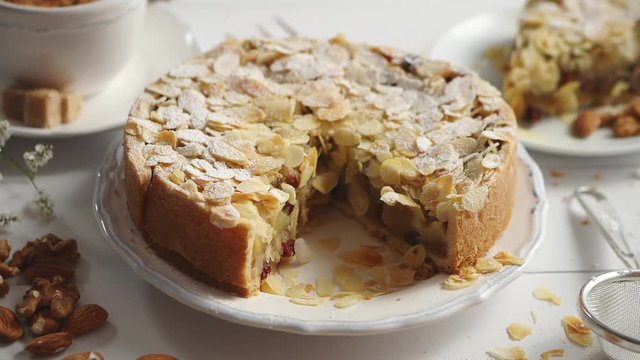 Shot of a whole round delicious apple cake tart with almond flakes served on wooden table. With coffee in a cup and slice of a pie on soucer.
