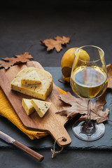 A glass of white wine served with cheese in a cutting board on dark background