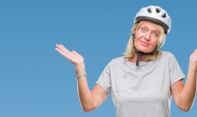 Middle age caucasian cyclist woman wearing safety helmet over isolated background clueless and confused expression with arms and hands raised. Doubt concept.