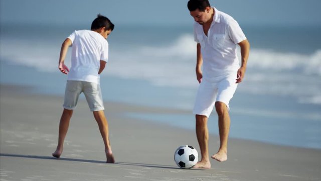 Hispanic father and son playing soccer ball on beach vacation