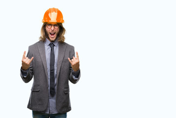 Young handsome architec man with long hair wearing safety helmet over isolated background shouting with crazy expression doing rock symbol with hands up. Music star. Heavy concept.