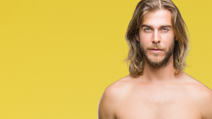 Young handsome shirtless man with long hair showing sexy body over isolated background with serious expression on face. Simple and natural looking at the camera.