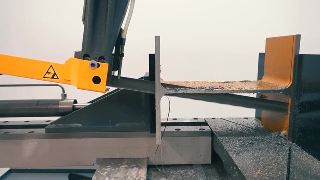 An industrial machine with a band saw accurately and qualitatively cuts a metal profile - an I-beam. Shot in motion
