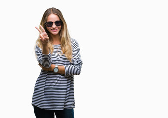 Fototapeta premium Young beautiful blonde woman wearing sunglasses over isolated background smiling with happy face winking at the camera doing victory sign. Number two.