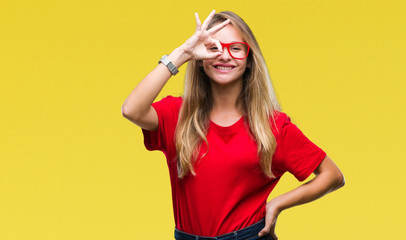 Young beautiful blonde woman wearing glasses over isolated background doing ok gesture with hand smiling, eye looking through fingers with happy face.