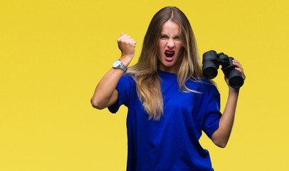 Young beautiful blonde woman looking through binoculars over isolated background annoyed and frustrated shouting with anger, crazy and yelling with raised hand, anger concept