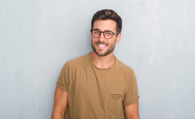 Handsome young man over grey grunge wall wearing glasses looking away to side with smile on face,...