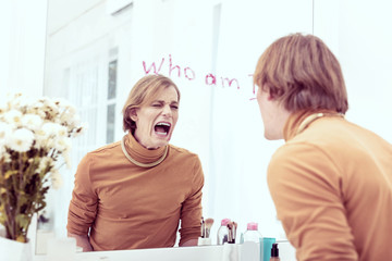 Transgender woman yelling at mirror with lipstick scrawl