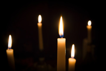 A number of burning melted candles with blurred forks of flame against dark background