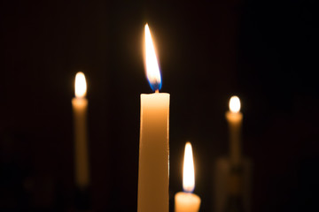 A number of burning melted candles with blurred forks of flame against dark background