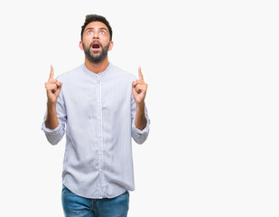 Fototapeta premium Adult hispanic man over isolated background amazed and surprised looking up and pointing with fingers and raised arms.