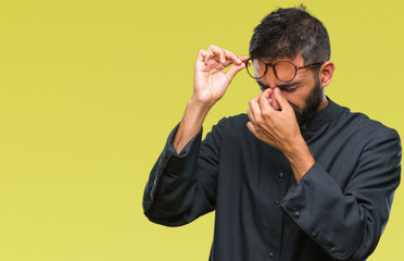 Adult hispanic catholic priest man over isolated background tired rubbing nose and eyes feeling...