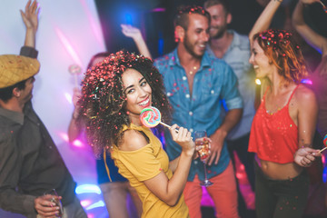 Group of friends dancing and drinking champagne at nightclub - Young happy people having fun and enjoying party eating candy lollipops - Youth friendship lifestyle concept