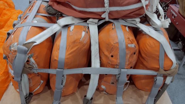 On the wooden pallet there are several orange bags with things and equipment fastened with a strap and with a laid parachute on top, ready to be dropped from an airplane. Shot in motion