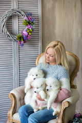 Blond woman posing with husky puppy white color in retro studio shoot on royal armchair. Cute young lady play with puppy dogs in designed home decorations.