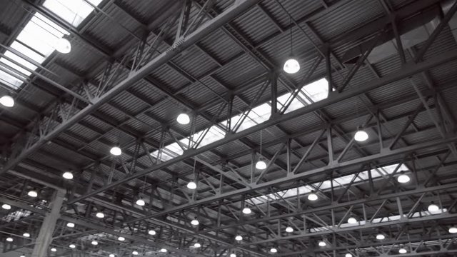 Hangar ceiling with many structural beams, ventilation pipes and luminous lamps. Shot in motion
