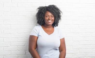 Young african american plus size woman over white brick wall with a happy and cool smile on face. Lucky person.