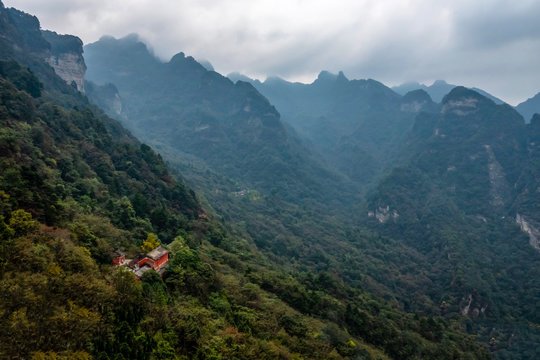 Red Taoist monastery and temple built on the side of a mountain with fall foliage and lush vegetation surrounding, in China