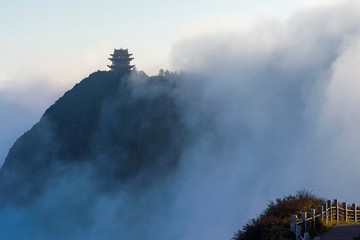 Chinese Buddhist temple peeking out from behind the fog and clouds on top of tall mountain in China