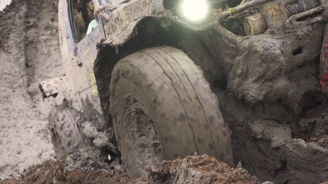 Close-up of the wheel of a car stuck in dirty water and dirt. The wheel turns, but it's helpless . electric winch pulls through the mud