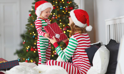 happy family mother hug her baby son  in pajamas opening gifts on christmas morning near   tree
