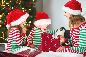 happy family mother and children in pajamas opening gifts on christmas morning near   tree