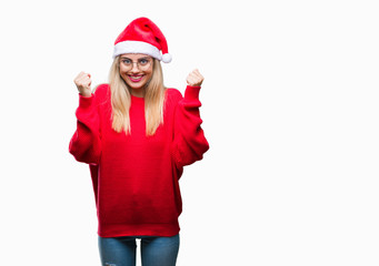 Young beautiful blonde woman wearing christmas hat over isolated background celebrating surprised and amazed for success with arms raised and open eyes. Winner concept.