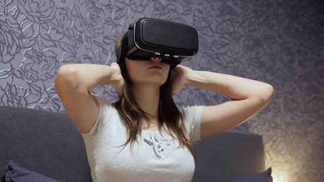 Beautiful young woman wearing VR Headset at bedroom. Looking around. Watch VR video, play VR game. Virtual reality concept. Close-up