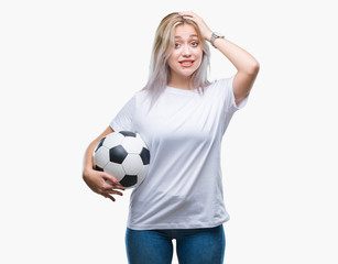 Young blonde woman holding soccer football ball over isolated background stressed with hand on head, shocked with shame and surprise face, angry and frustrated. Fear and upset for mistake.