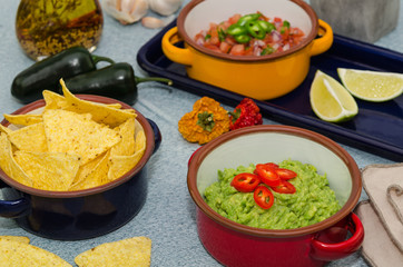 Guacamole and salsa dip next to tortilla chips. A delicious bowl of guacamole next to fresh ingredients on a table with tortilla chips and salsa. 