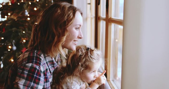 Mother and Daughter Having Fun on Christmas Morning. SLOW MOTION. Precious family moment, young mom playing with her toddler daughter by the window, winter landscape. 