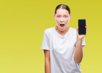 Young beautiful caucasian woman showing smartphone screen over isolated background scared in shock with a surprise face, afraid and excited with fear expression