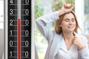 High temperature on thermometer and woman suffering from heat in office