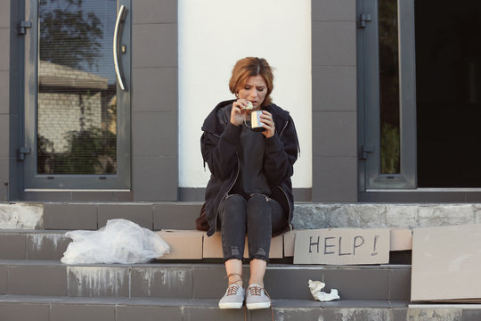 Poor woman with piece of bread and mug on city street