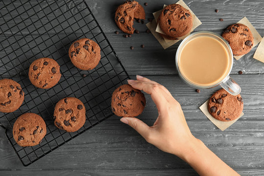 Woman Taking Tasty Chocolate Chip Cookie From Cooling Rack On Wooden Background, Top View