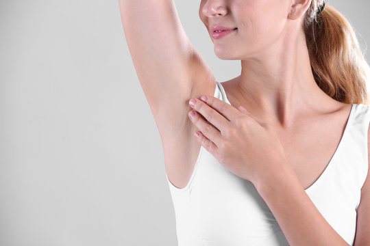 Young woman showing armpit on grey background, space for text. Using deodorant
