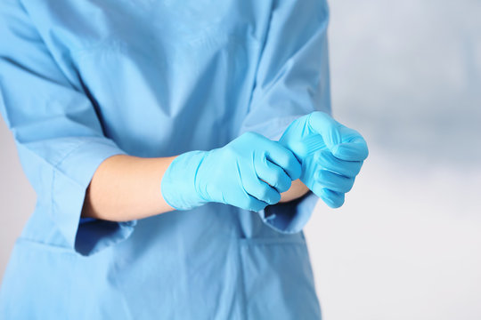 Doctor taking off medical gloves on color background