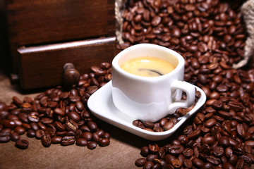 Fresh roasted coffee beans in burlap sack, coffee cup and grinder on dark background.