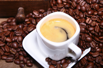 Fresh roasted coffee beans in burlap sack, coffee cup and grinder on dark background.