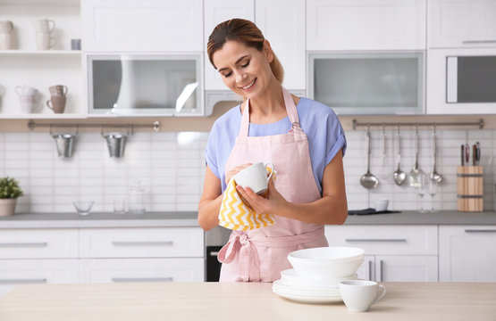 Woman wiping ceramic cup at table with clean dishes in kitchen