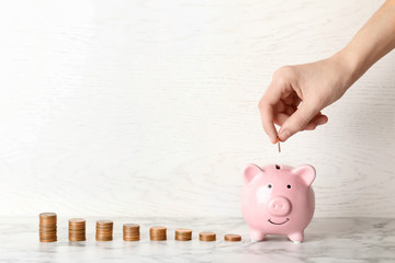 Woman putting coin into piggy bank against light background. Space for text