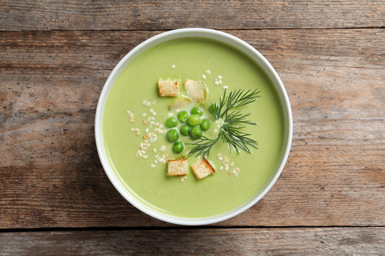 Fresh vegetable detox soup made of green peas with croutons in dish on wooden background, top view